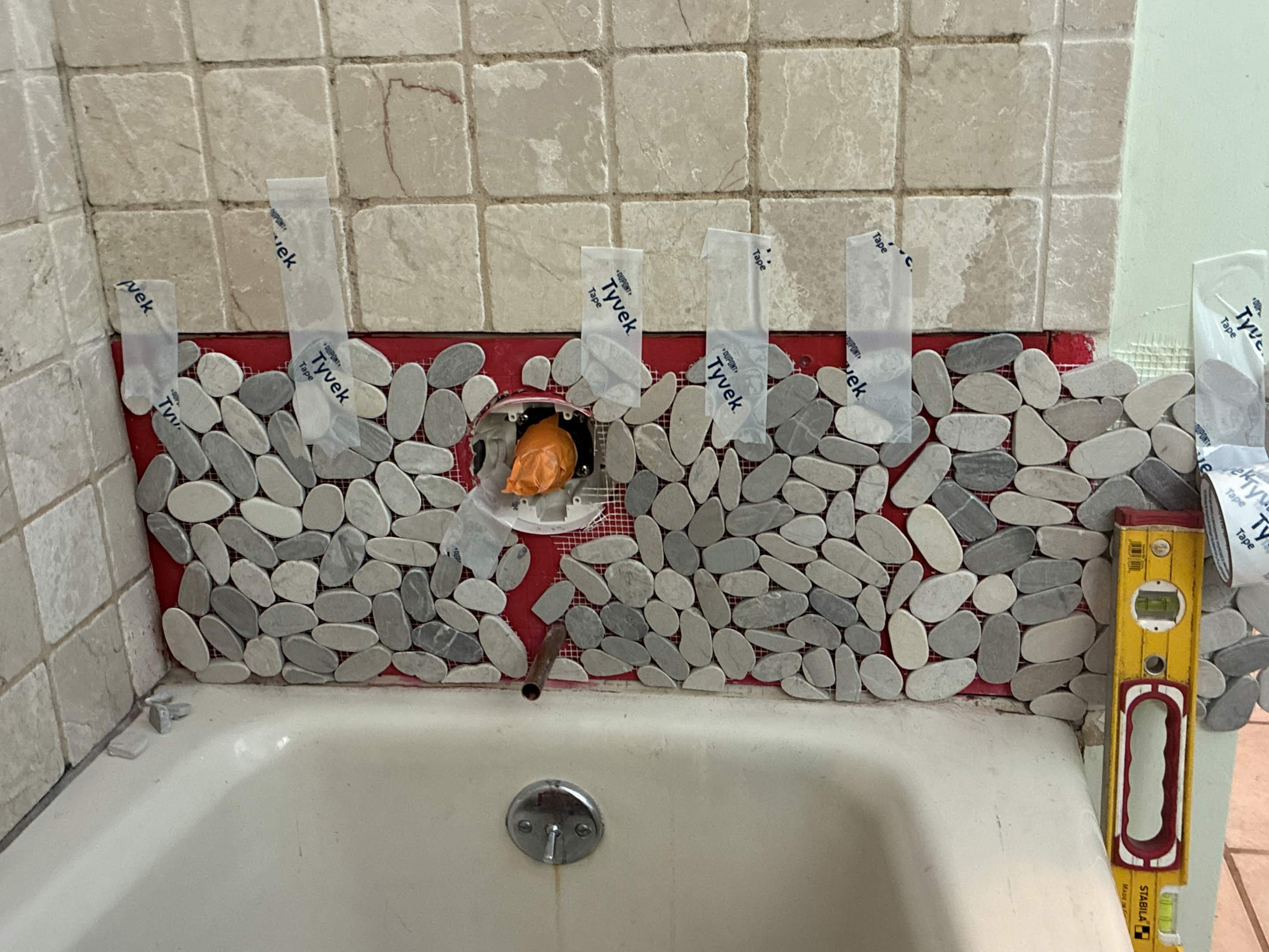 Pebble mosaic accent band leveled across the tub surround during tile install