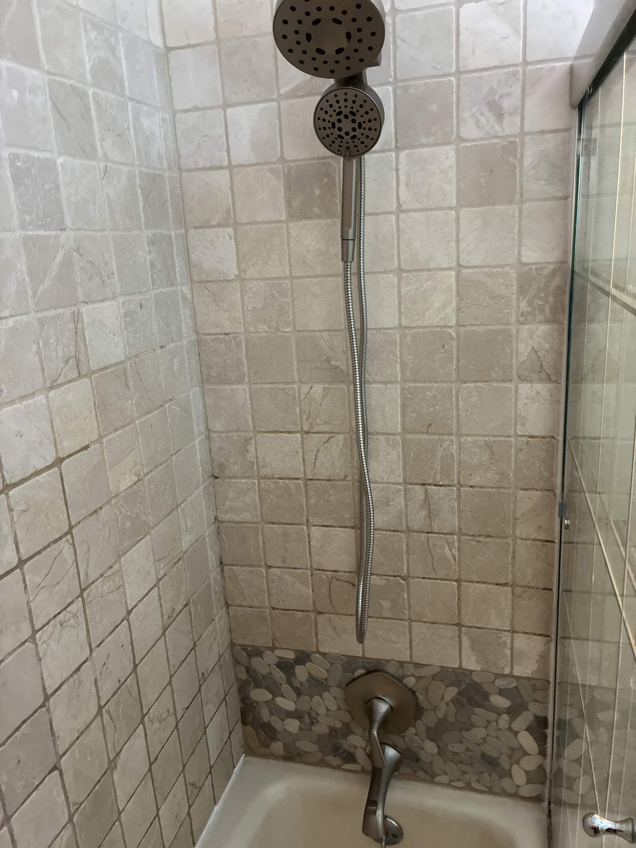 Finished shower with travertine tile, handheld showerhead, and pebble-mosaic accent band